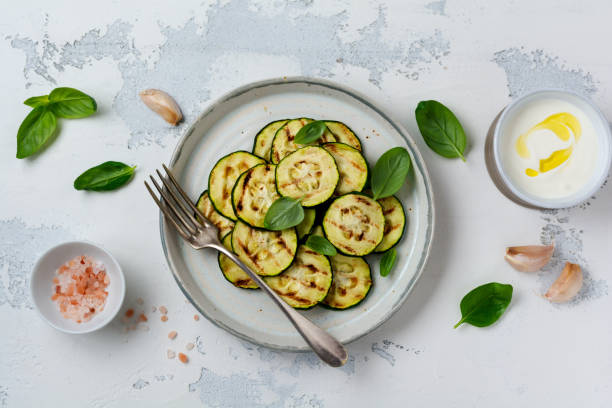 istock Grilled zucchini salad with basil leaves, yogurt sauce and fried bread in a simple ceramic plate on a white concrete background. Flat lay with copy space. 1165120010