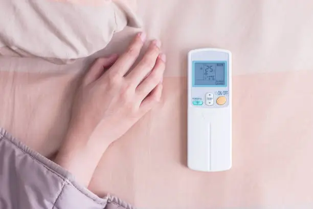 Woman hand under blanket with remote control air-conditioner.