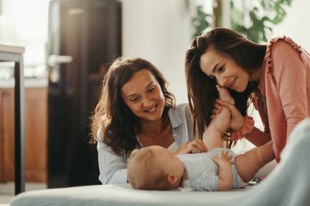 Affectionate women enjoying in time with a baby son at home. Loving lesbian couple playing with their baby while spending time together at home. lgbtqia rights photos stock pictures, royalty-free photos & images