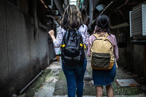 Rear view of Two unrecognizable students walking in alley  with backpacks