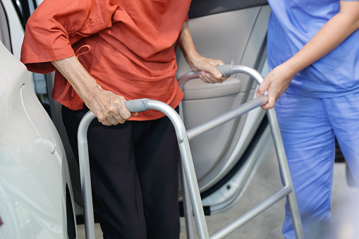 Elderly female using walker while get out of car with caregiver