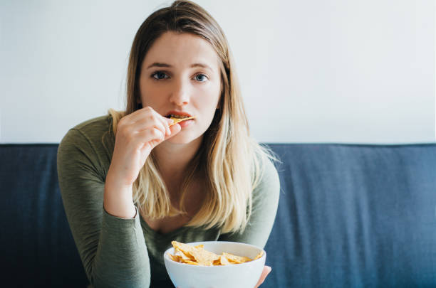 istock Young woman eating snacks on the couch 1165129977