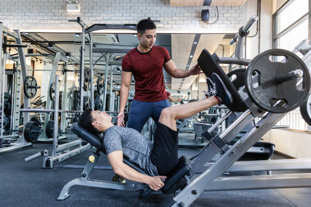 istock Young Asian man working on his leg push workout program with his male trainer at a gym 1165131866