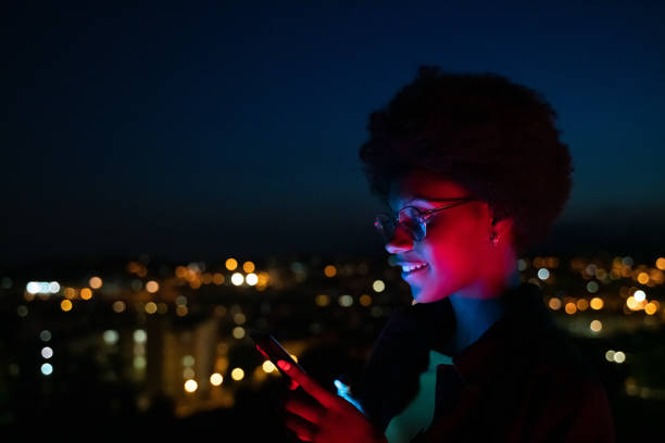 Young woman using her mobile phone at night with the city at background stock photo