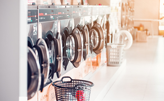 Row of industrial laundry machines in laundromat  in a public laundromat, with laundry in a basket , Thailand