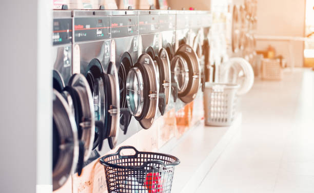 Row of industrial laundry machines in laundromat  in a public laundromat, with laundry in a basket , Thailand Row of industrial laundry machines in laundromat  in a public laundromat, with laundry in a basket , Thailand laundry stock pictures, royalty-free photos & images