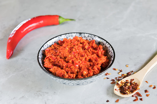 Traditional Maghrebi hot chili pepper sauce harissa on a grey marble background. Arabic cuisine. Adjika Hot Pepper Sauce. Peperoncini calabrese with olive oil, close up, copy space