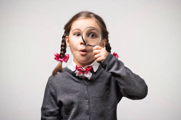 istock Child Girl Student Looking Through Magnifying Glass on Grey Background with Available Copy Space. Back to School Concept. 1165140713