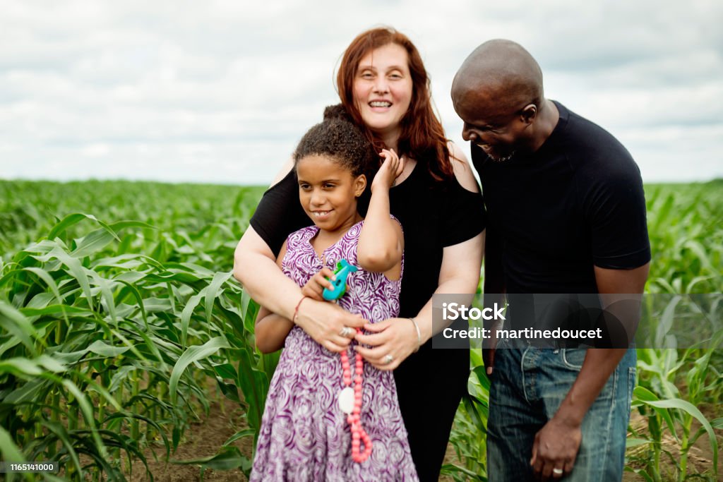 Portrait of mixed-race family with autist daughter in nature. A young autist girl is posing for a family portrait with her mother and father in a corn field. She is holding small plastic toys to comfort herself in new situations that can be stressful. Mixed-race family. Horizontal waist up outdoors shot with copy space. Autism Stock Photo