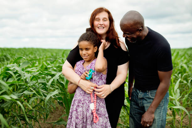 Portrait of mixed-race family with autist daughter in nature. A young autist girl is posing for a family portrait with her mother and father in a corn field. She is holding small plastic toys to comfort herself in new situations that can be stressful. Mixed-race family. Horizontal waist up outdoors shot with copy space. autism photos stock pictures, royalty-free photos & images