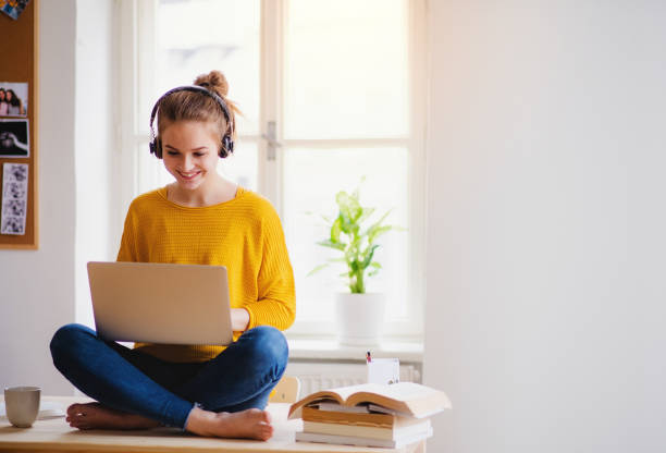 a young female student sitting at the table, using headphones when studying. - furniture internet adult blond hair imagens e fotografias de stock