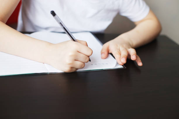 istock the boy sits at the table and writes in a notebook. child sits and does homework on a white background 1165143185