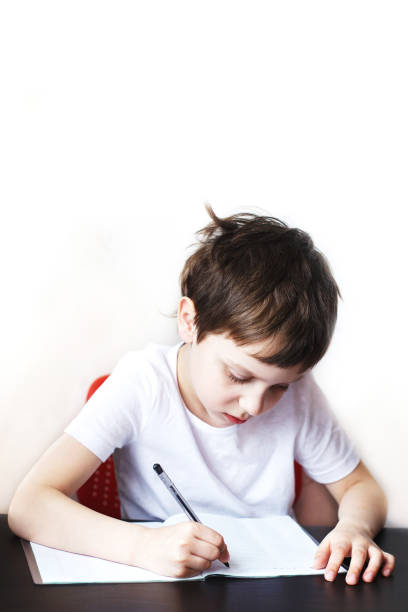istock the boy sits at the table and writes in a notebook. child sits and does homework on a white background 1165143216