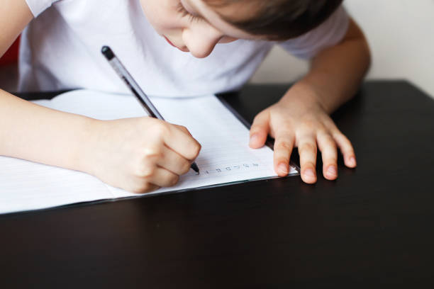 istock the boy sits at the table and writes in a notebook. child sits and does homework on a white background 1165143267