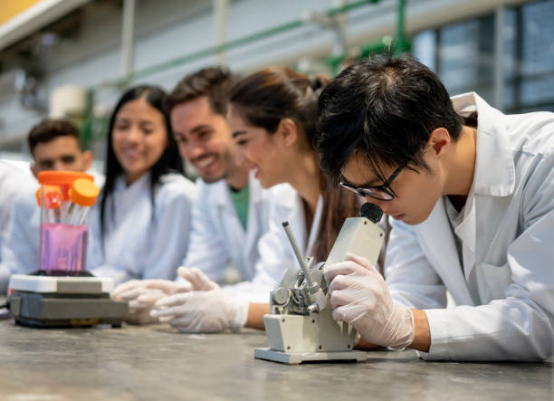 istock Asian student looking at something with a microscope during a biology class and other students at background 1165145539