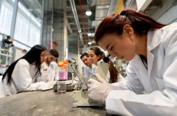 istock Female student looking at something on microscope and chemistry students at the back experimenting with liquids at college 1165145611