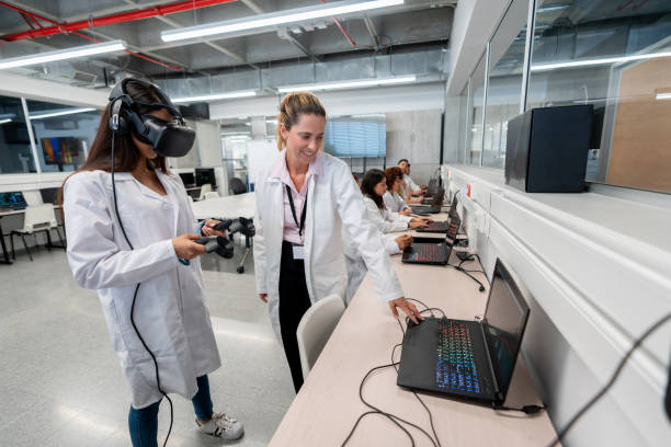istock Adult female teacher using laptop while student experiments with virtual reality simlator and joysticks 1165145631