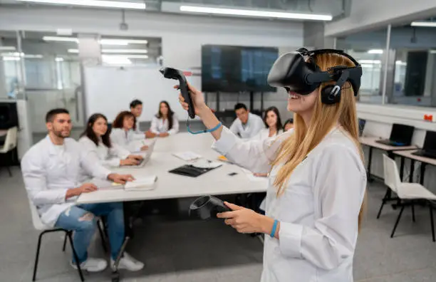 Students at college doing an experiment watching a student while using virtual reality headset and joysticks smiling