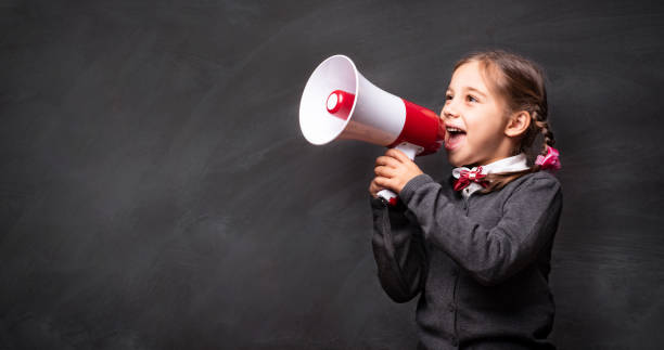 child girl student shouting through megaphone on blackboard backdrop with available copy space. back to school concept. - marketing megaphone child using voice imagens e fotografias de stock