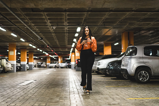 Young woman walking and using smartphone at parking lot