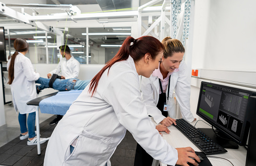 Female teacher and student looking at a program on desktop at the biomechanics lab - Incidental students at background