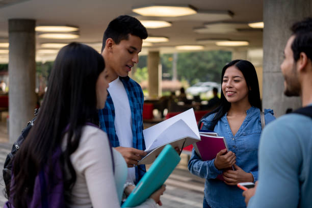 istock Group of college buddies standing next to partner reading something on notebook at college 1165150772