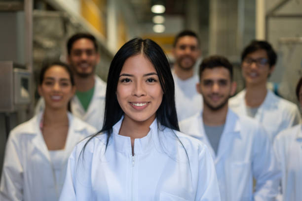 young female pharmaceutical student smiling at camera and group of friends standing at background - smiling research science and technology clothing imagens e fotografias de stock