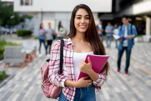 retrato de una estudiante latinoamericana bonita sosteniendo sus cuadernos mientras mira la cámara sonriendo en su campus universitario - men latin american and hispanic ethnicity young men smiling fotografías e imágenes de stock