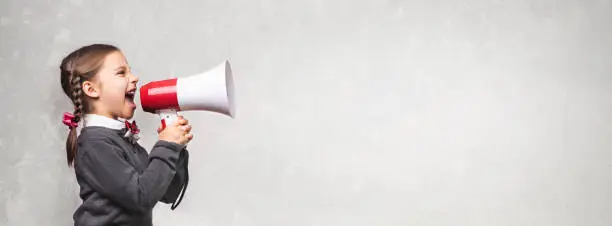 Photo of Child Girl Student Shouting Through Megaphone on Grey Backdrop with Available Copy Space. Back to School Concept.