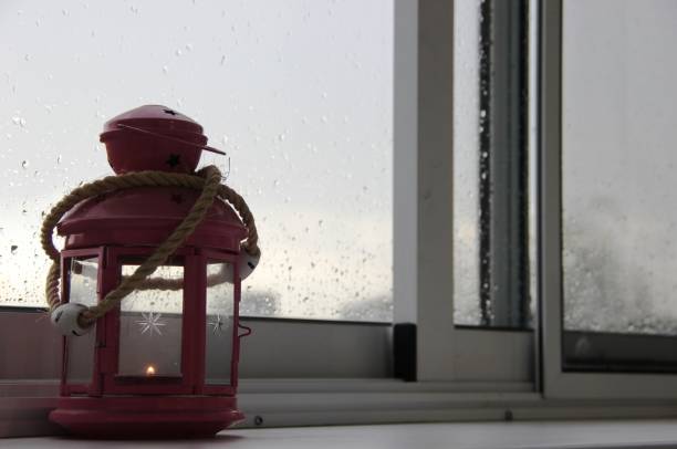 istock rainy summer day, raindrops on the window glass, decorative pink lantern with a burning candle inside, houses on the PVC window 1165153256