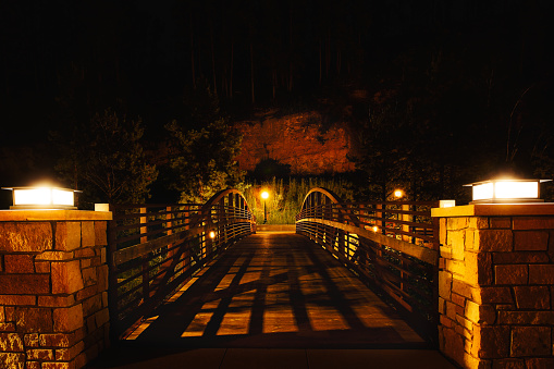 A wooden pedestrian bridge illuminated by solar lights surrounded by trees and rock wall in a nighttime South Dakota landscape