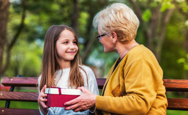 Grandchild surprised her grandmother with a birthday present in the park. Lifestyle, family concept Gift for a grandmother. Grandchild surprised her grandmother with a birthday present in the park. Lifestyle, family concept happy birthday cousin stock pictures, royalty-free photos & images