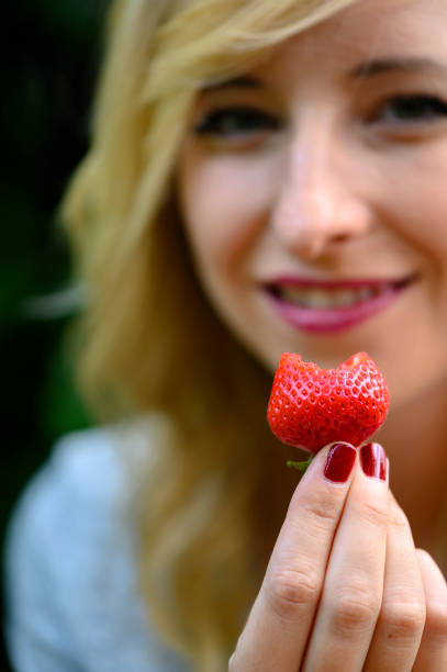 istock A ripe strawberry from which a young woman has bitten off. 1165166663