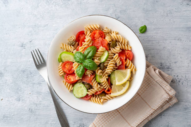 istock Whole wheat pasta salad with cucumbers, cherry tomatoes, salted salmon and capers on concrete background 1165170141