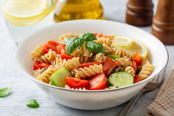 istock Whole wheat pasta salad with cucumbers, cherry tomatoes, salted salmon and capers on concrete background 1165170171