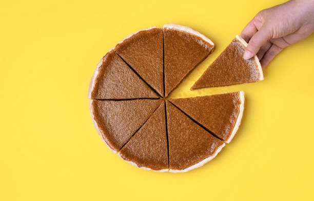Sliced pumpkin pie. Taking a pie slice. Woman hand holding and taking a piece of pumpkin pie on a yellow background. Above view of traditional autumn dessert. Thanksgiving sweet food. Eating pie. sweet pie stock pictures, royalty-free photos & images