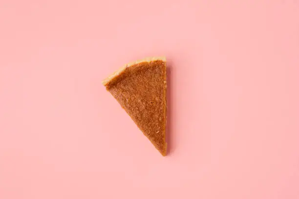 Traditional pumpkin pie slice on pink paper background. Above view of one pie portion. Minimal image of the last pie slice. Thanksgiving dessert