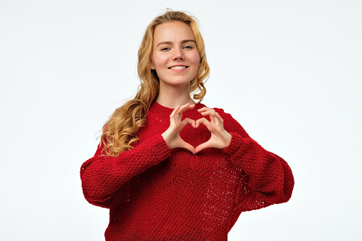 Young woman with long blonde hair making a heart with her hands