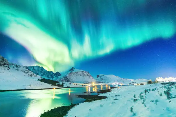 Photo of Amazing view on natural wonder Northern Lights or Aurora Borealis over lighting Kubholmenleia bridge crossing the fjord. Lofoten Islands Archipelago in Norway, location over Polar Circle.