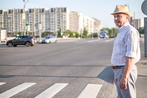 Mature man in summer hat waiting to cross street on sunny day.