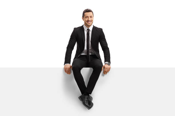 Young man in a suit sitting on a panel and smiling Full length portrait of a young man in a suit sitting on a panel and smiling isolated on white background sitting stock pictures, royalty-free photos & images
