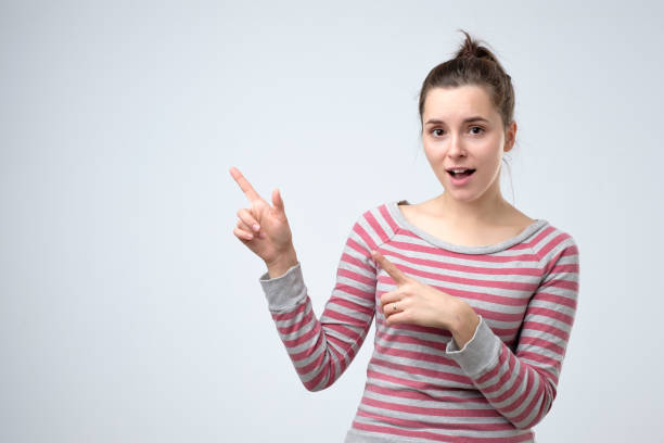 istock woman smiling broadly pointing fingers away, showing something interesting 1165185444