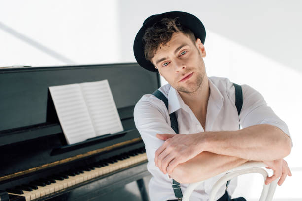 istock dreamy pianist in white shirt and black hat looking at camera 1165185848