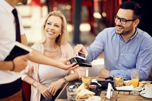 Happy man making easy payment with mobile phone while having a lunch with his girlfriend in a bar.