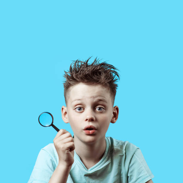istock a boy in a light t-shirt holding a small magnifying glass on blue background 1165189226