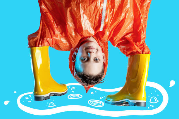 istock smiling boy in orange raincoat stuck his hands in rubber boots on blue background 1165189285