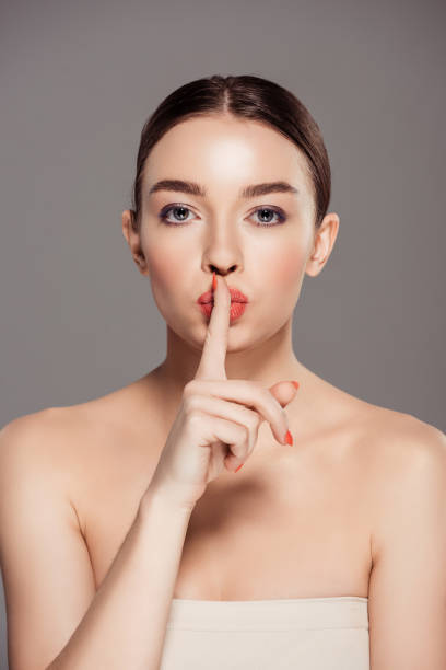 istock beautiful girl looking at camera and doing silent gesture isolated on grey 1165189663