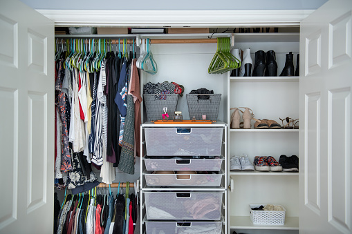 This is a female's closet with well organized shelves of purses, shoes and hanging clothes.