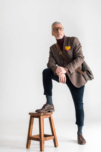 istock fashionable mature man putting leg on chair while standing on grey 1165195519