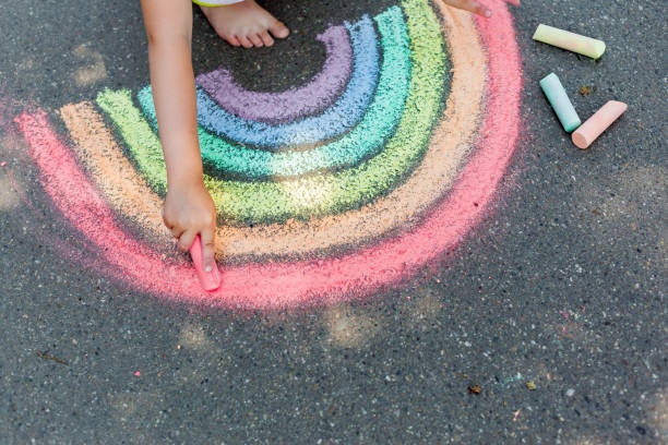 l'enfant dessine un arc-en-ciel avec de la craie colorée sur l'asphalte. concept de peintures de dessins d'enfant. éducation et arts, soyez créatif à la rentrée - dessin à la craie photos et images de collection